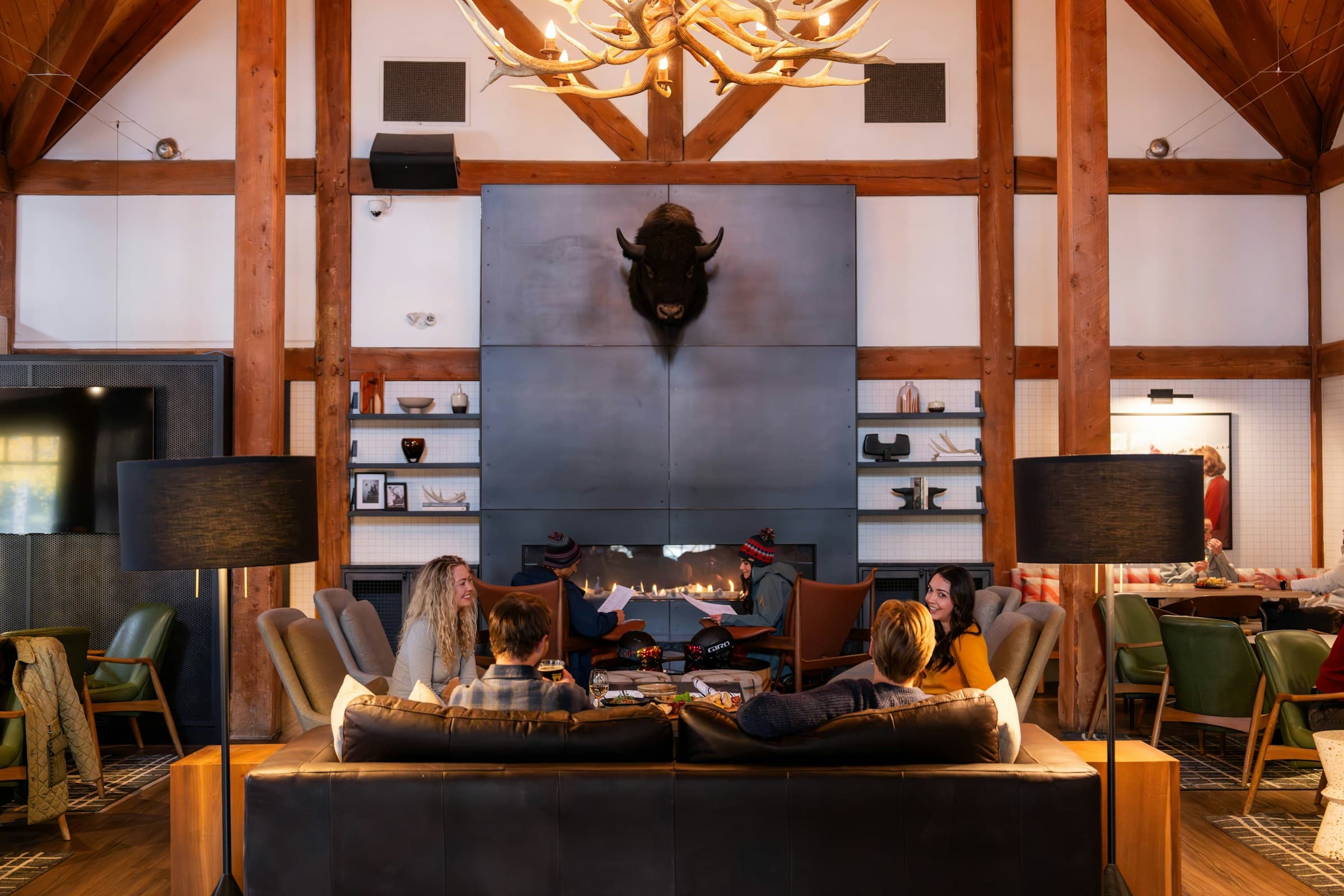 The lounge of a timber mountain lodge — open fire, leather seating, exposed trusses