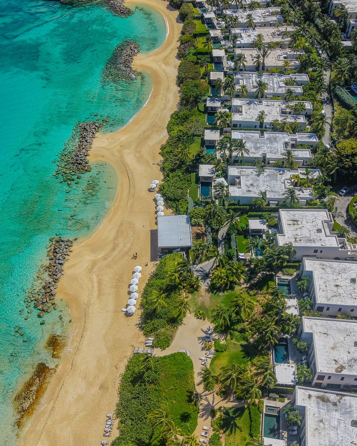 Villas with private pools along a turquoise bay, seen from the air
