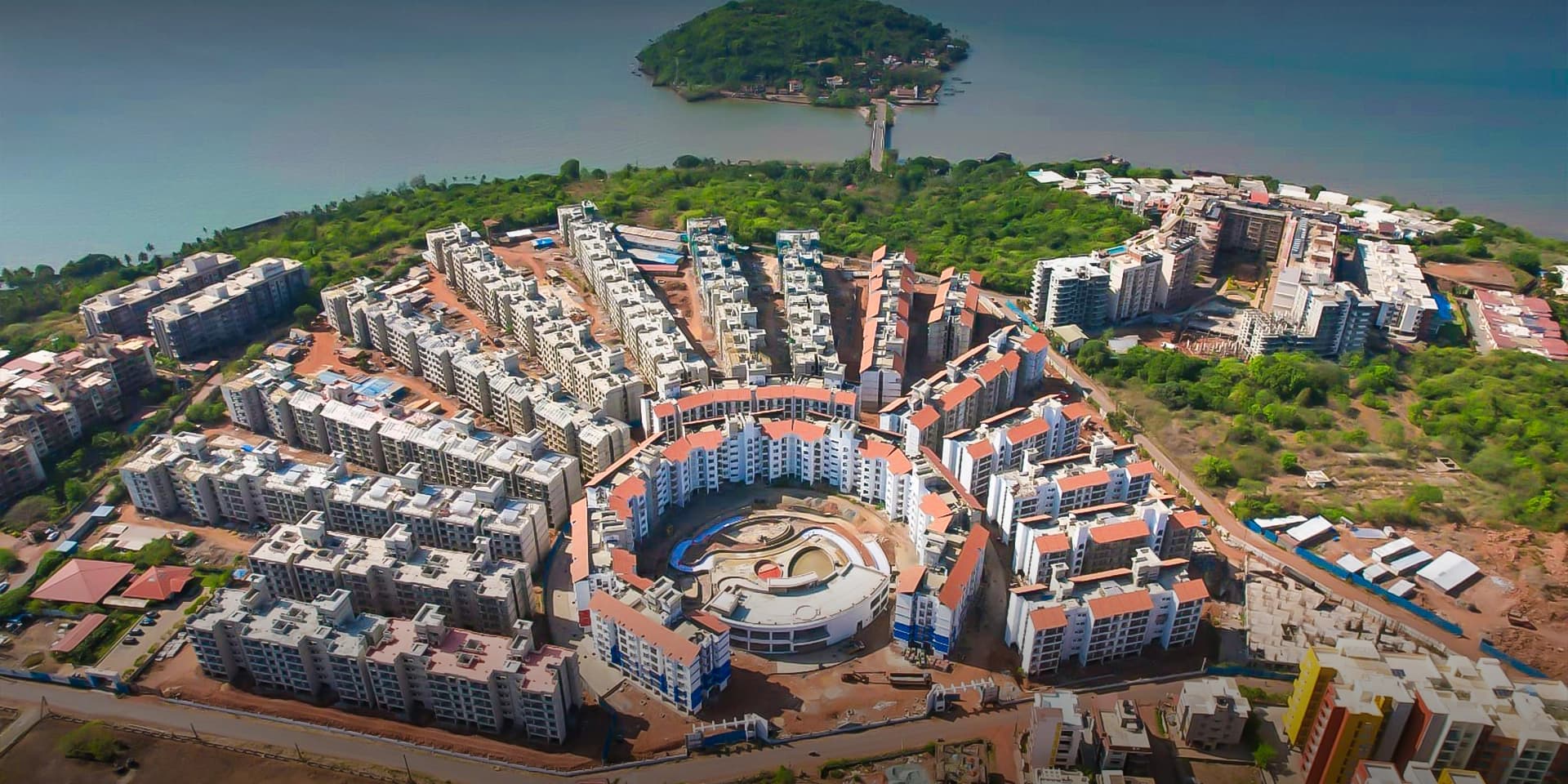 Adora De Goa from the air — condominium blocks around the central water amenity, with the estuary beyond